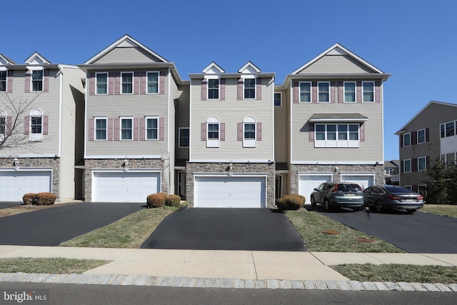 multi unit property with stone siding, a garage, and driveway