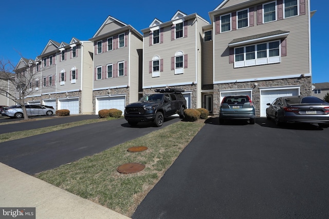 view of front of house with stone siding, a garage, a residential view, and driveway