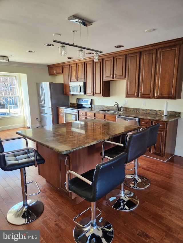 kitchen with a breakfast bar, dark wood finished floors, appliances with stainless steel finishes, a sink, and a kitchen island