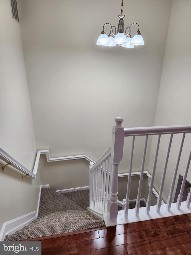 stairway with visible vents, hardwood / wood-style floors, baseboards, and an inviting chandelier