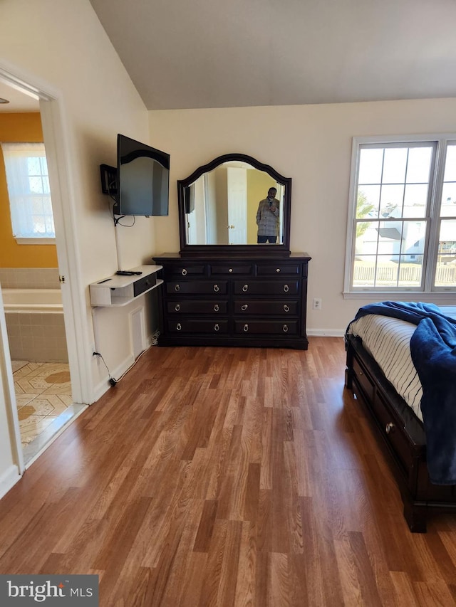 bedroom with lofted ceiling, connected bathroom, and wood finished floors