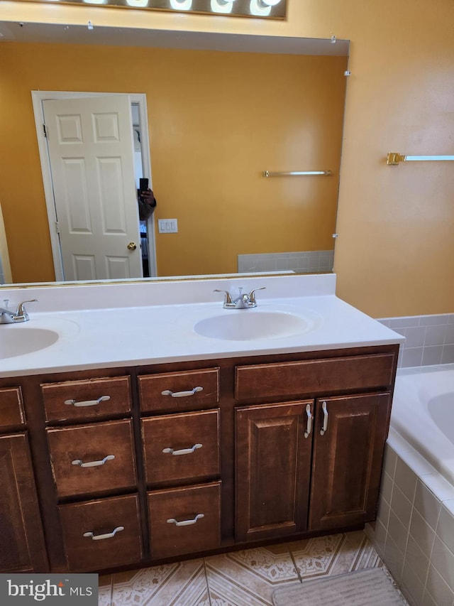 bathroom with double vanity, tiled tub, and a sink