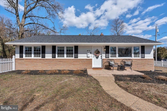 view of front of property with a shingled roof, stone siding, a chimney, fence, and a front yard