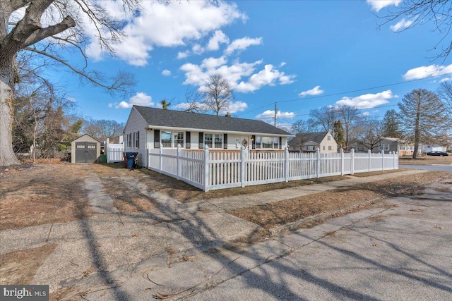 ranch-style home featuring a fenced front yard, roof with shingles, an outdoor structure, and a shed