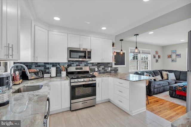 kitchen with a peninsula, a sink, white cabinets, open floor plan, and appliances with stainless steel finishes