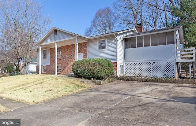 view of front of house featuring brick siding, a chimney, a front yard, and a sunroom