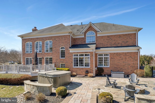 back of house with a patio, brick siding, a chimney, and a hot tub