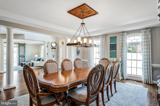 dining room featuring ornate columns, a barn door, ornamental molding, and wood finished floors