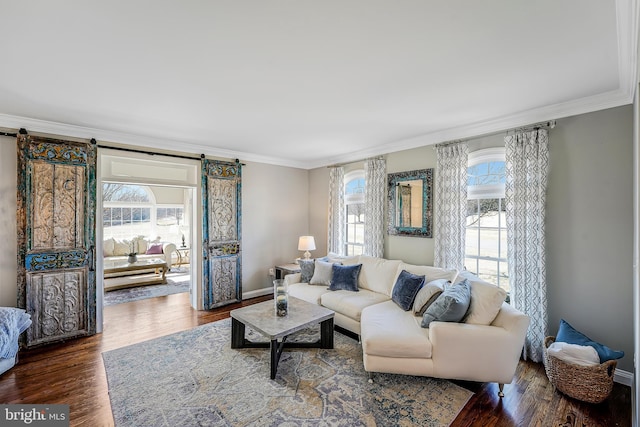 living area with a barn door, a healthy amount of sunlight, wood finished floors, and crown molding