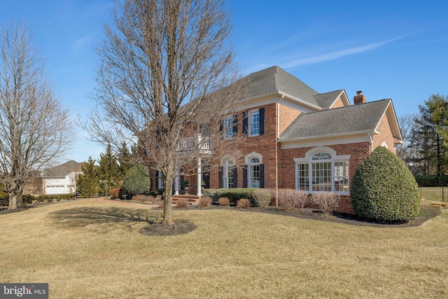 view of front of home featuring a chimney, brick siding, a balcony, and a front lawn