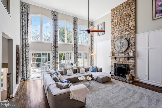 living area with a decorative wall, a fireplace, wood finished floors, a ceiling fan, and ornamental molding