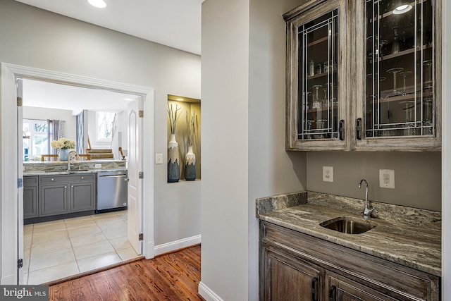 bar with baseboards, light tile patterned flooring, dishwasher, and a sink