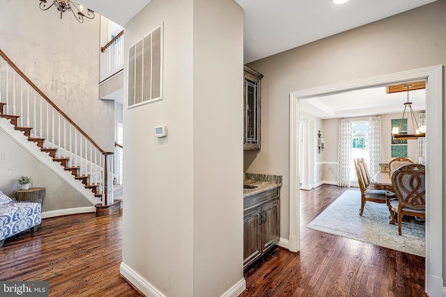 corridor with dark wood-style floors, visible vents, stairway, an inviting chandelier, and baseboards