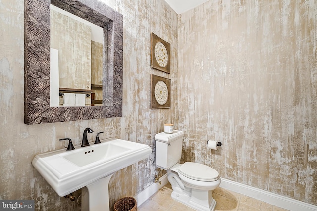 half bath with baseboards, a sink, toilet, and tile patterned floors