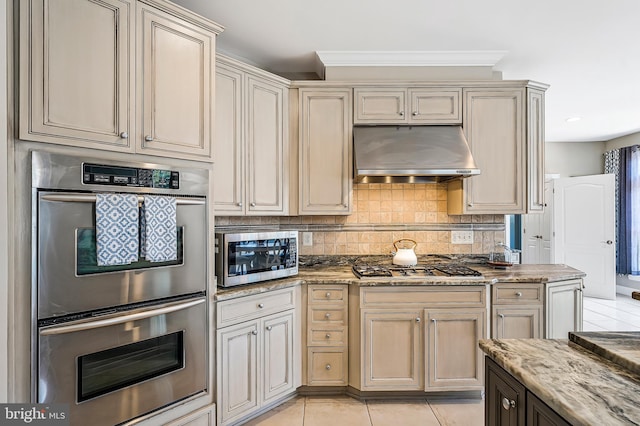 kitchen with stainless steel appliances, decorative backsplash, under cabinet range hood, and cream cabinets