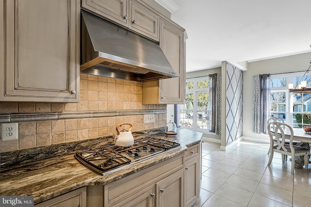 kitchen featuring light stone counters, under cabinet range hood, stainless steel gas cooktop, backsplash, and light tile patterned flooring