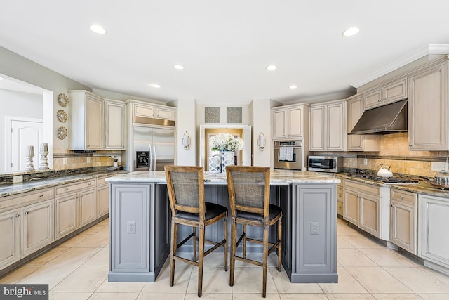 kitchen featuring a breakfast bar area, light tile patterned floors, cream cabinets, appliances with stainless steel finishes, and under cabinet range hood