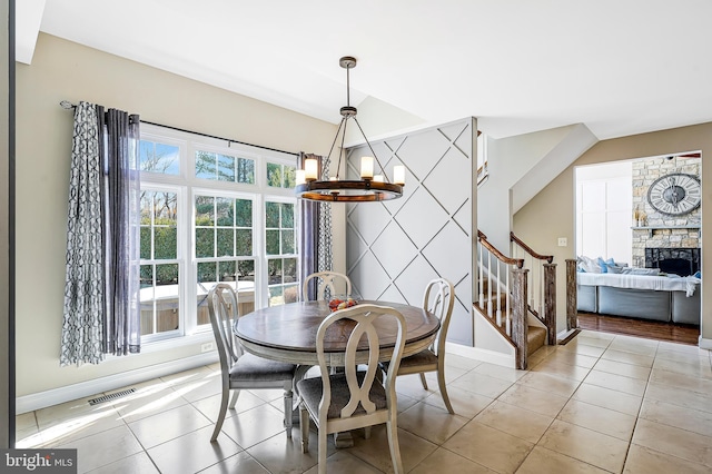 tiled dining area with a notable chandelier, a fireplace, visible vents, an accent wall, and stairs