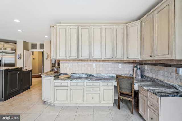 kitchen with light tile patterned floors, built in desk, decorative backsplash, and stainless steel built in fridge