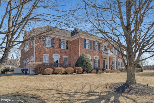 colonial-style house with a balcony, a front lawn, and brick siding