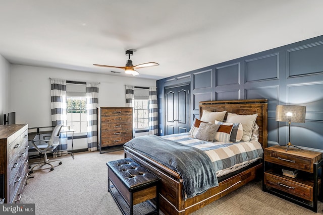 bedroom with ceiling fan, light colored carpet, and a decorative wall