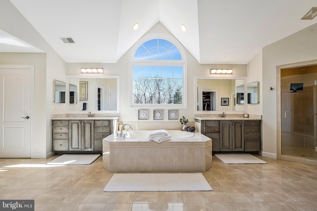 bathroom with a garden tub, visible vents, vaulted ceiling, and a sink