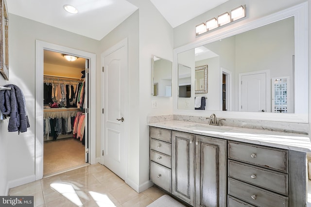 bathroom with tile patterned flooring, a spacious closet, baseboards, and vanity