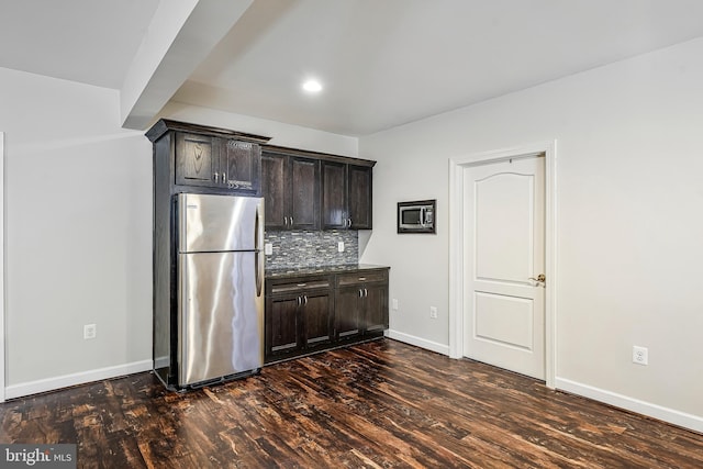 kitchen with dark brown cabinets, dark wood-style flooring, backsplash, and freestanding refrigerator