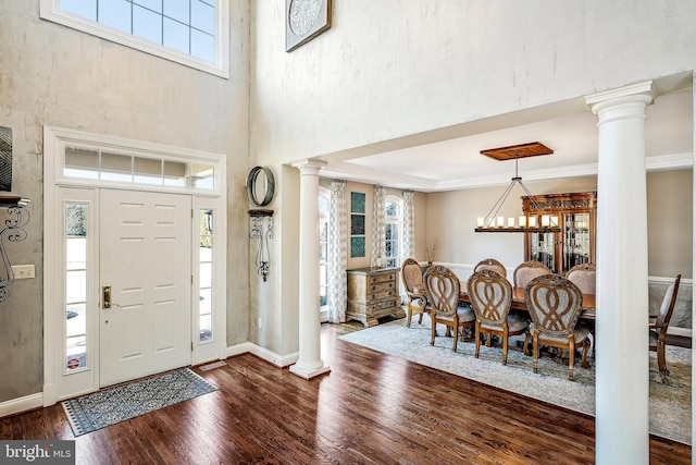 entrance foyer with dark wood-type flooring, plenty of natural light, crown molding, and decorative columns