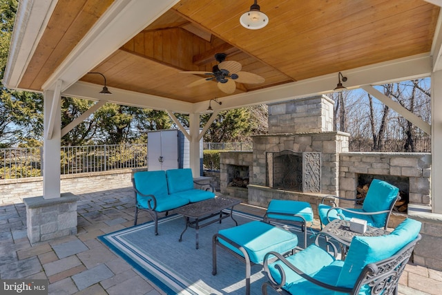 view of patio featuring a ceiling fan, fence, and an outdoor living space with a fireplace