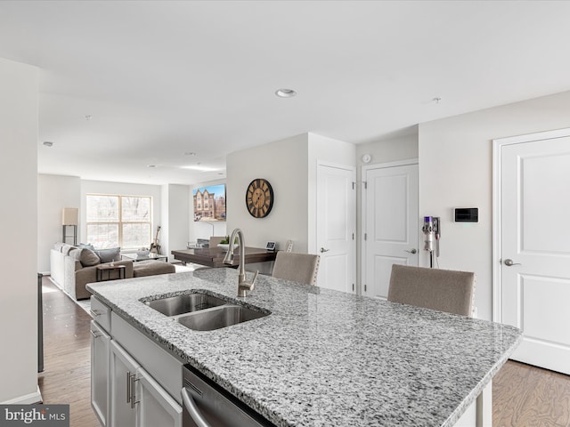 kitchen featuring light stone counters, light wood-type flooring, a sink, and an island with sink