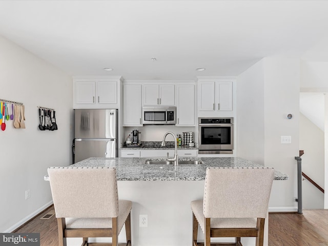 kitchen featuring a breakfast bar area, a sink, white cabinets, appliances with stainless steel finishes, and dark wood finished floors