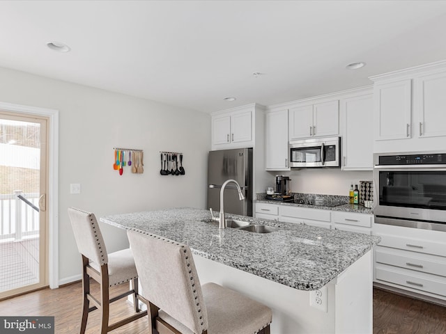 kitchen with wood finished floors, appliances with stainless steel finishes, a sink, and a center island with sink