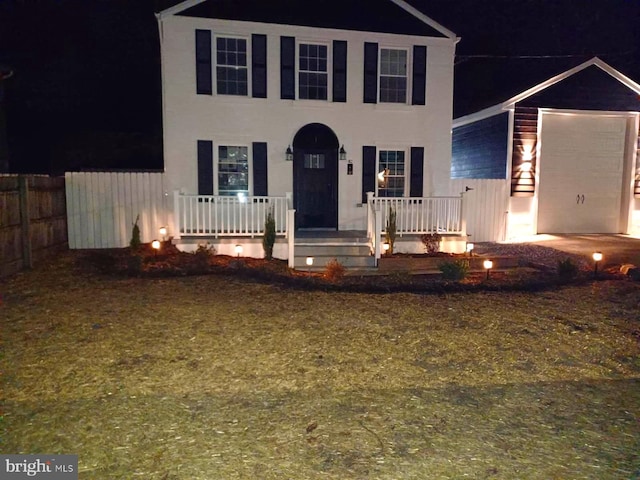 colonial-style house featuring a porch, fence, and stucco siding