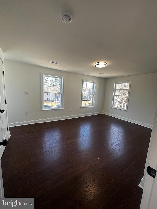 unfurnished room with dark wood-type flooring, visible vents, and baseboards