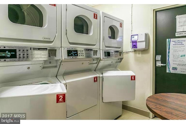 community laundry room featuring stacked washer / dryer, light tile patterned flooring, washing machine and dryer, and baseboards