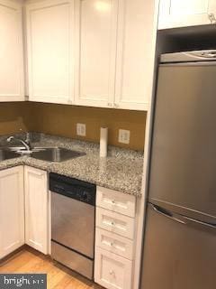 kitchen with stainless steel dishwasher, light wood-style floors, white cabinetry, a sink, and fridge