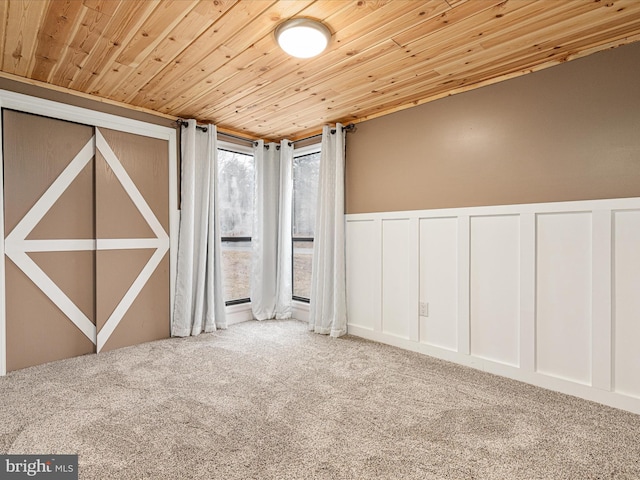 carpeted spare room with wainscoting, wood ceiling, and a decorative wall