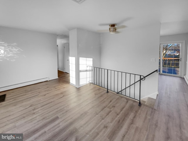 unfurnished room featuring a baseboard heating unit, ceiling fan, and wood finished floors