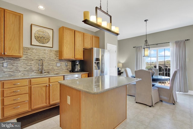 kitchen with a sink, light stone counters, a kitchen island, appliances with stainless steel finishes, and decorative backsplash