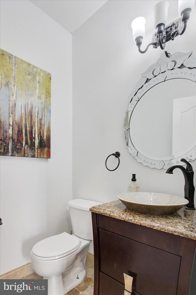 half bath with vanity, a notable chandelier, toilet, and baseboards