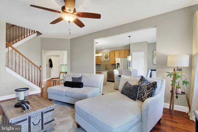 living area with stairs, baseboards, light wood finished floors, and ceiling fan