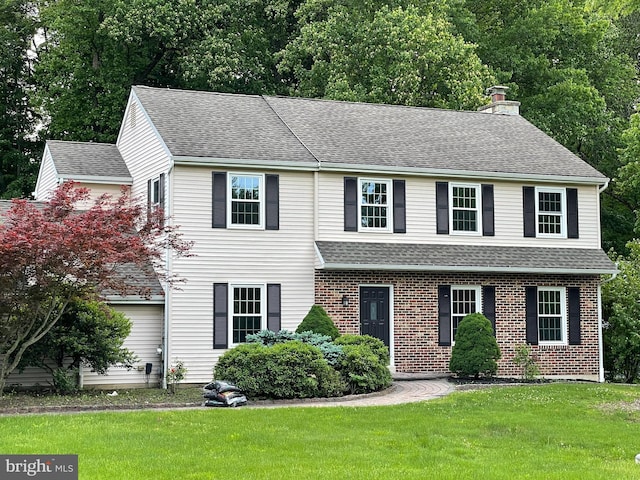 view of front of home featuring a chimney, brick siding, roof with shingles, and a front yard