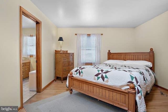 bedroom featuring baseboards, ensuite bathroom, and light wood-style floors