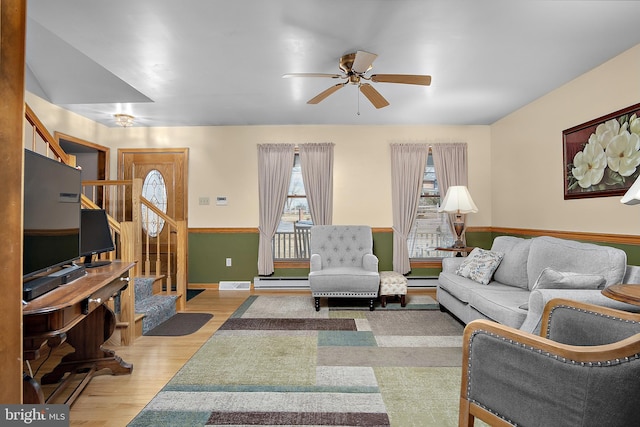 living room with a ceiling fan, stairway, baseboard heating, and wood finished floors