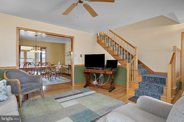 living area featuring ceiling fan with notable chandelier, stairway, baseboards, and wood finished floors