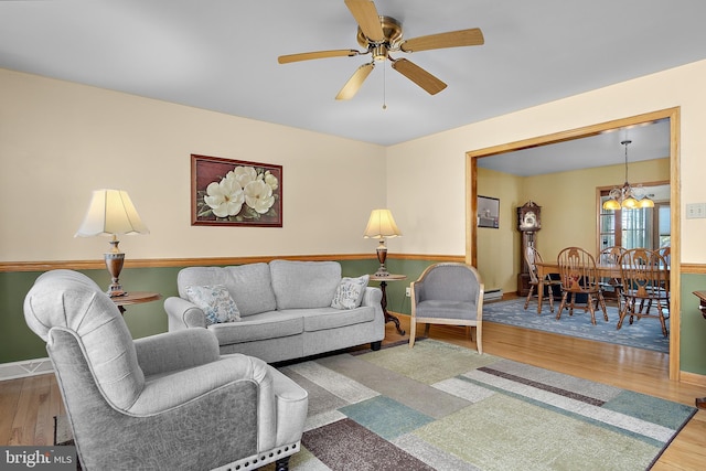 living room with ceiling fan with notable chandelier, a baseboard radiator, baseboards, and wood finished floors