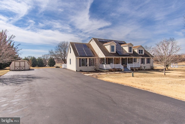 cape cod house featuring solar panels, a porch, a storage shed, an outdoor structure, and driveway