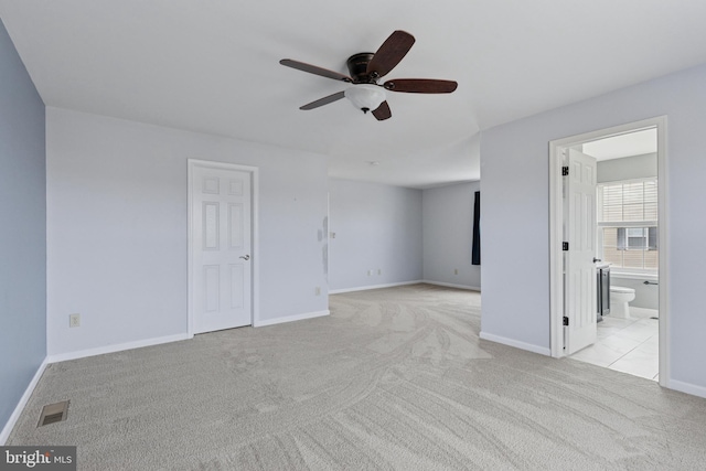 unfurnished bedroom featuring ceiling fan, light colored carpet, visible vents, baseboards, and ensuite bath