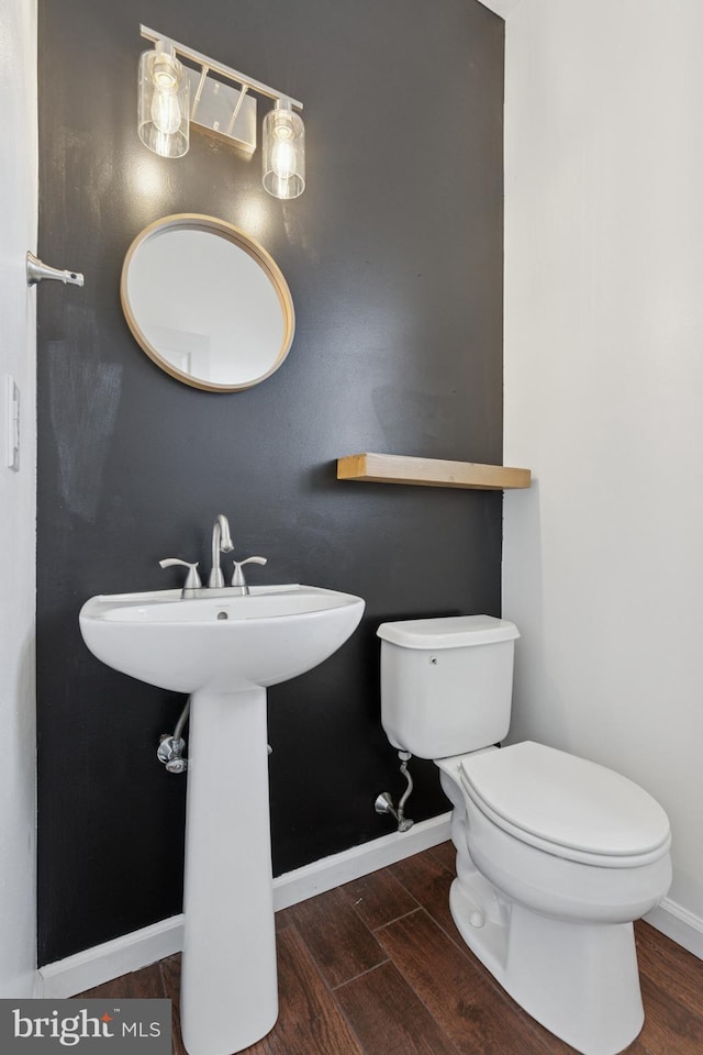 half bathroom featuring wood finished floors, toilet, and baseboards